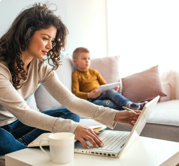 woman looking on computer on couch next to child