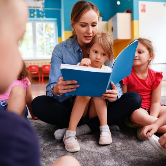 teacher reading to a little girl on her lap in group