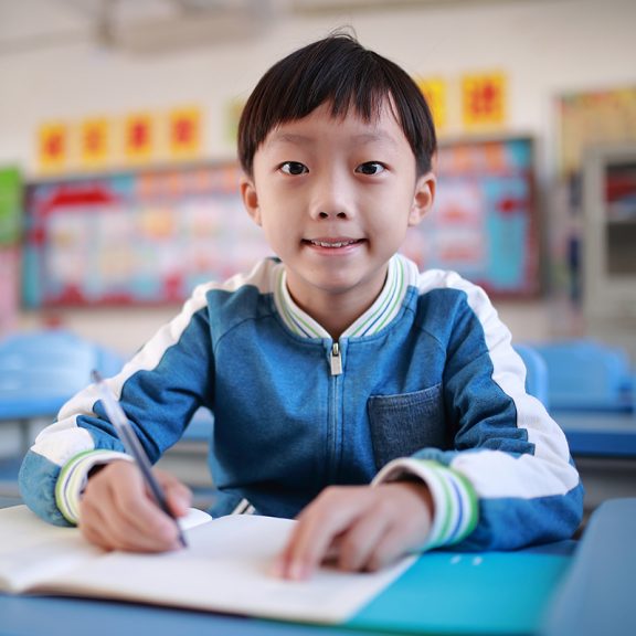 little boy writing at school desk smiling