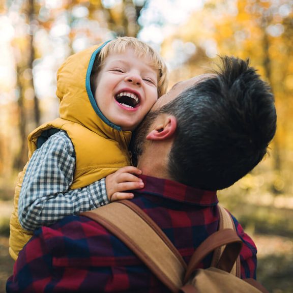 man carrying child in the woods making them laugh and smile