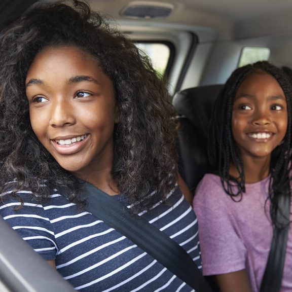 two girls riding in back of automobile looking out window smiling