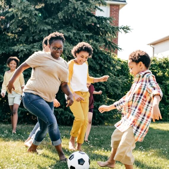 woman playing soccer in yard with kids