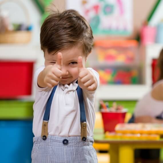 little boy in classroom giving two thumbs up smiling